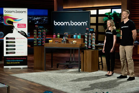 Two BoomBoom founders presenting nasal sticks on the Shark Tank stage with a product display and boom.boom logo on screen