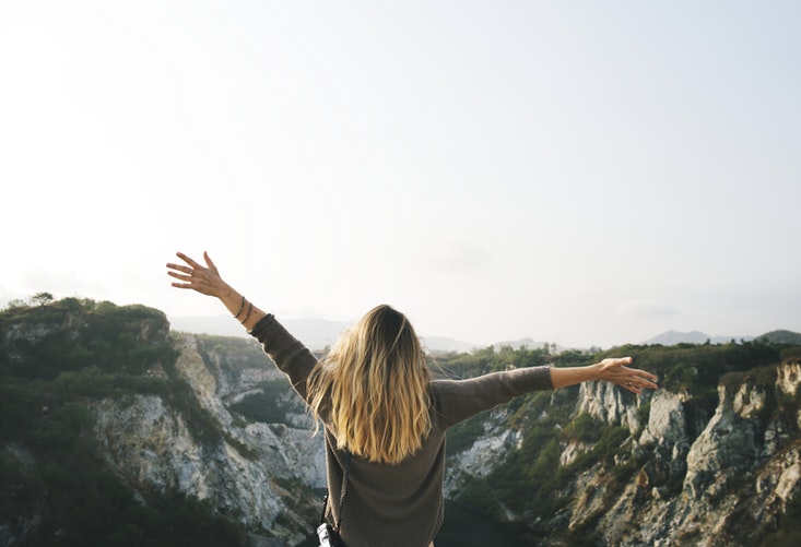 Woman standing on a cliff with arms outstretched, overlooking a rocky valley and evoking a refreshing reset
