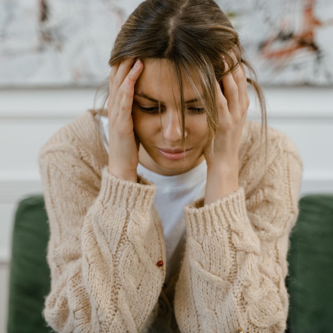Woman holding her head and looking down on a couch, appearing fatigued and contemplative