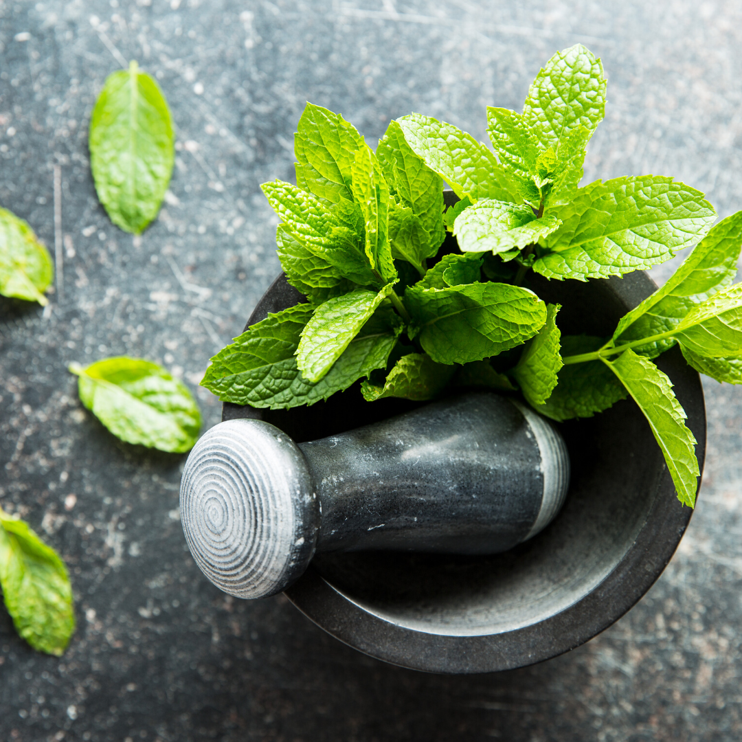 Fresh mint leaves with a stone pestle in a mortar on a dark textured surface, suggesting menthol freshness