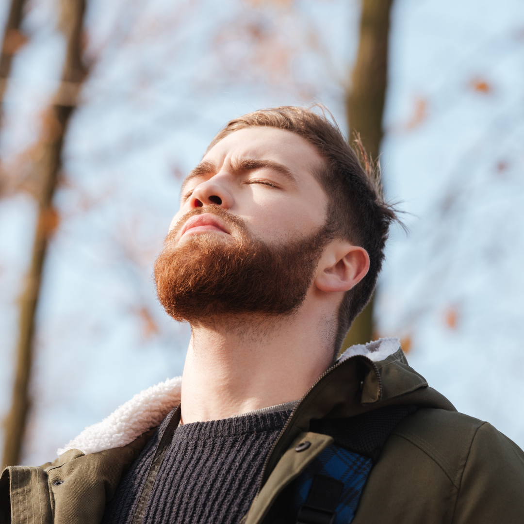 Young bearded man breathing deeply with eyes closed outdoors in a jacket under bare trees
