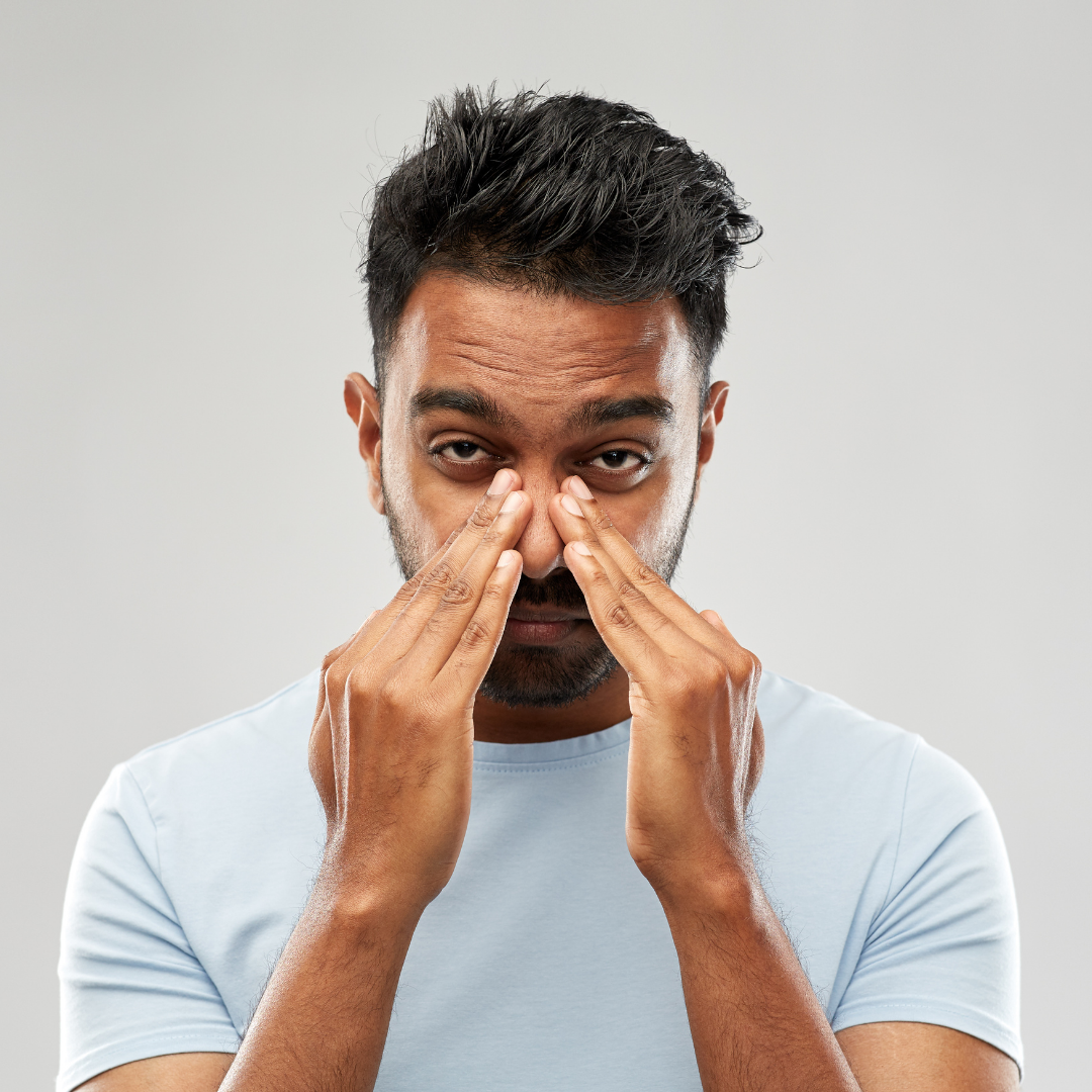 Man pressing the bridge of his nose in discomfort, indicating sinus congestion against a plain gray background