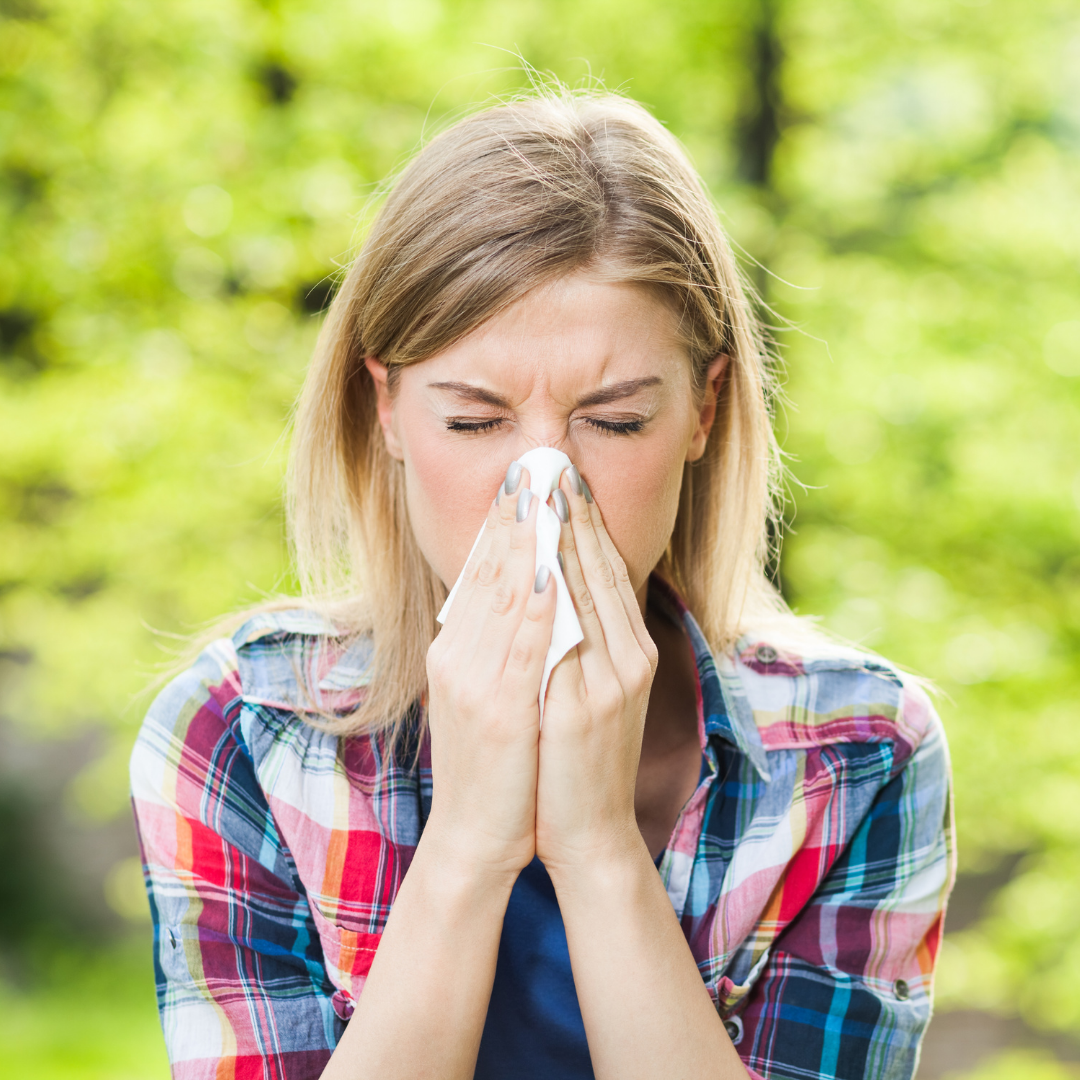 Woman sneezing into a tissue outdoors with a blurred green background