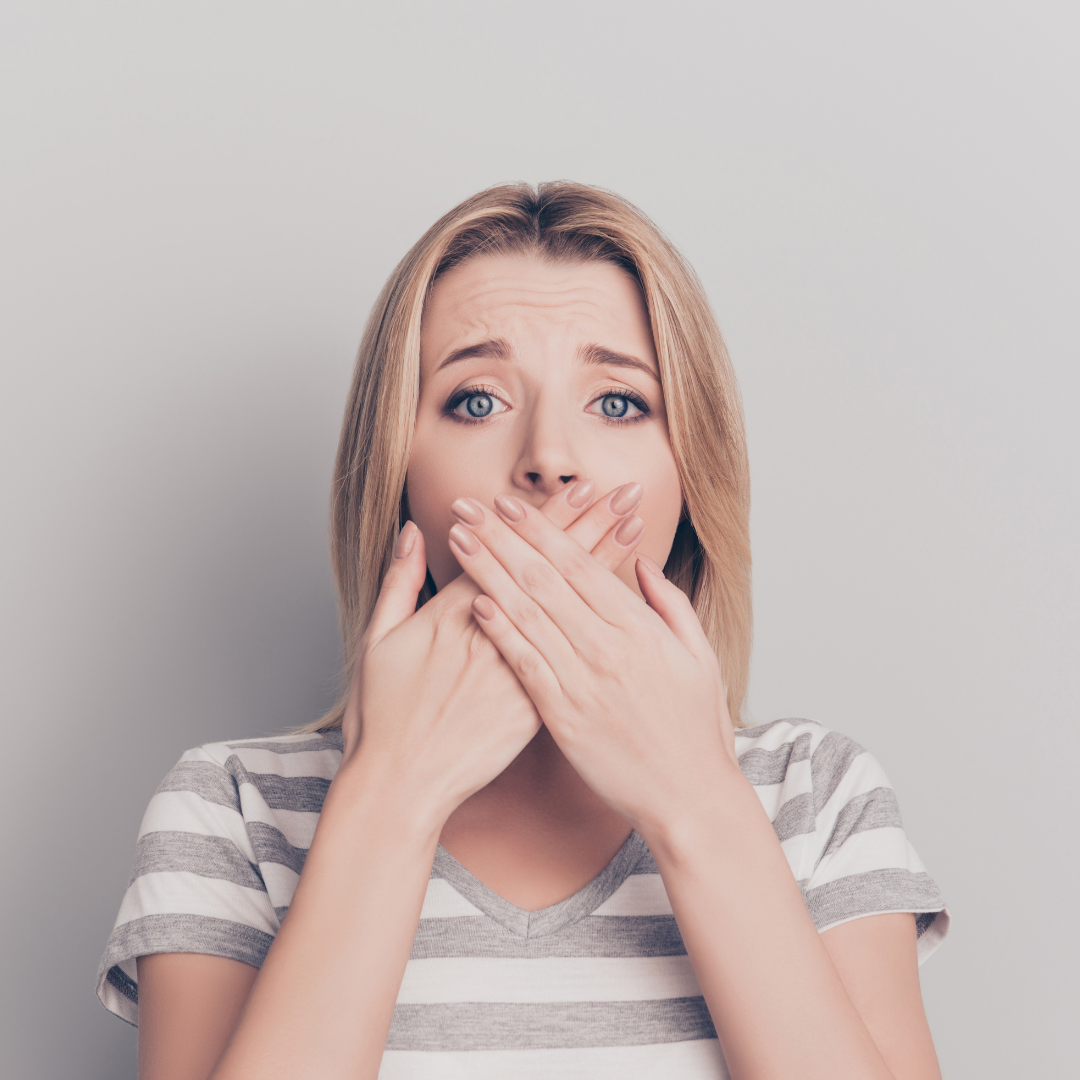 Woman covering her mouth with both hands, looking nauseous against a plain light gray background