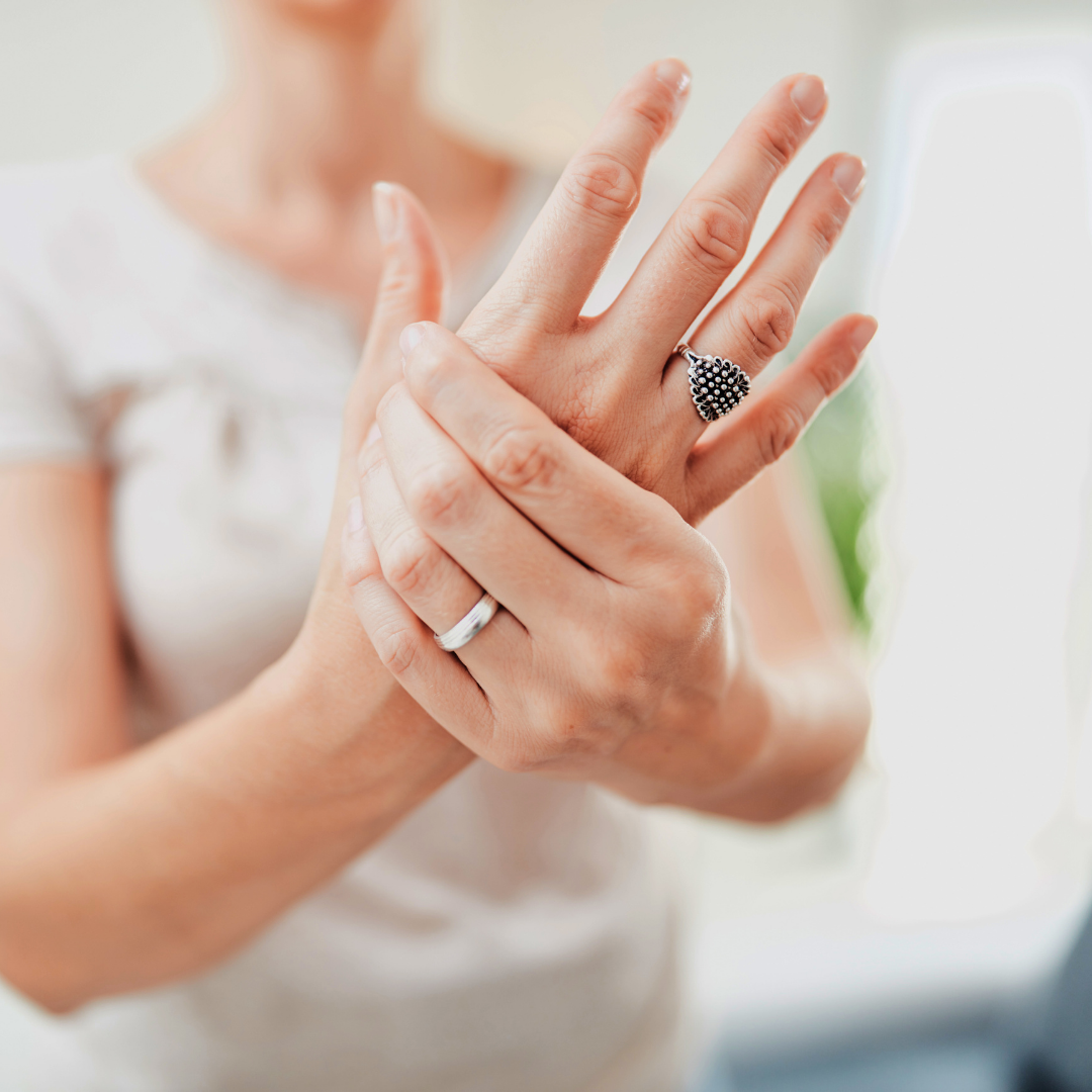 Close-up of a person gently massaging their hands, suggesting hand pain or neuropathy relief in a softly lit indoor setting