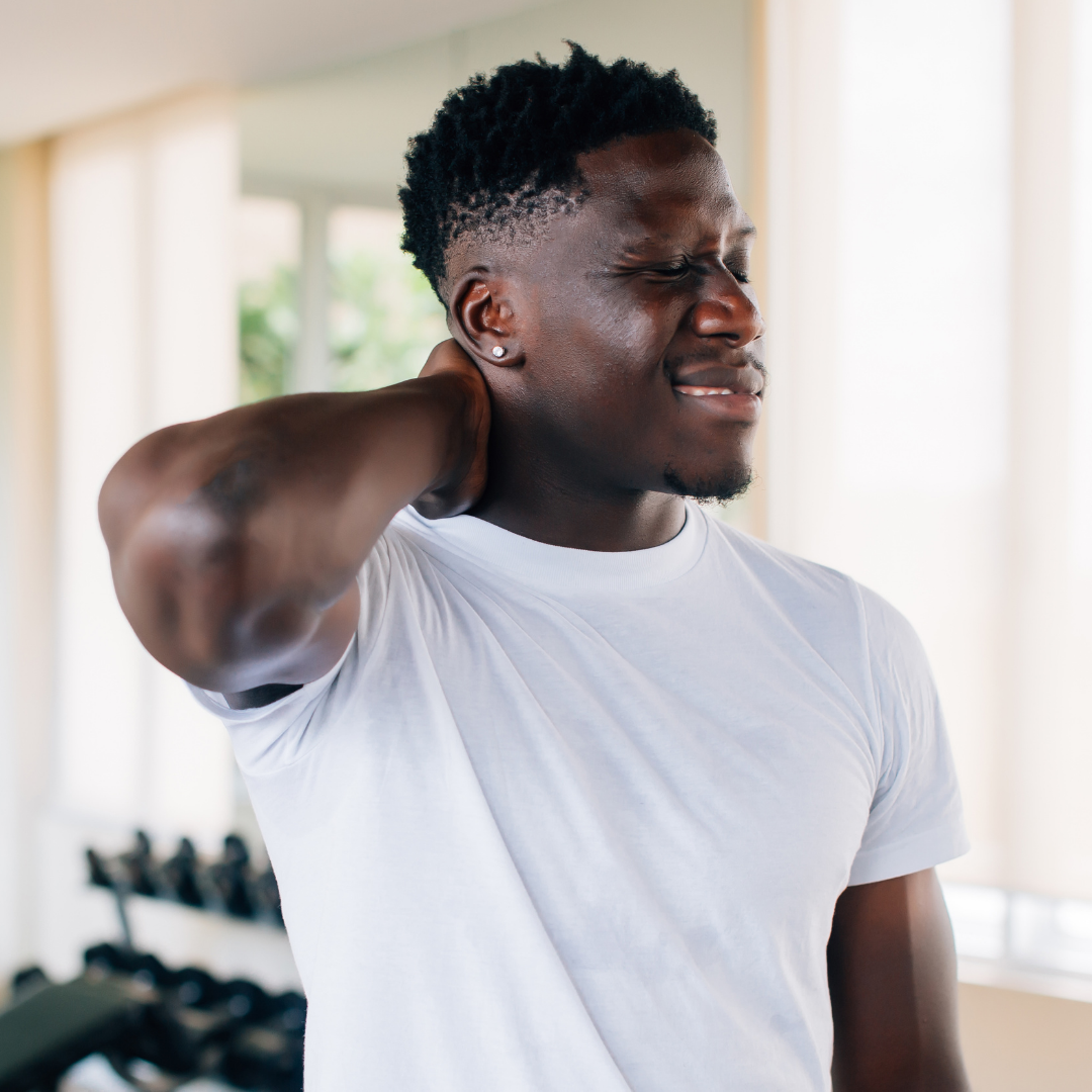 Man rubbing his neck in pain in a bright room with dumbbells visible in the background