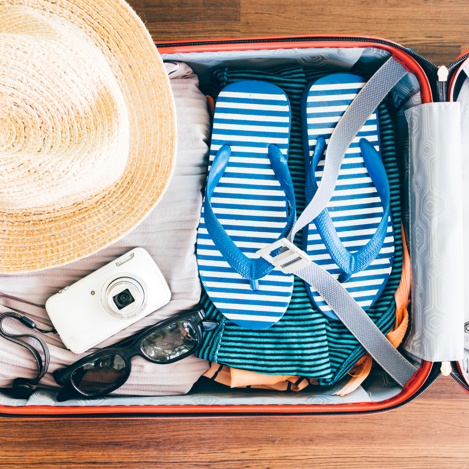 Top-down view of open suitcase with a straw sun hat, blue striped flip-flops, a white camera, and sunglasses