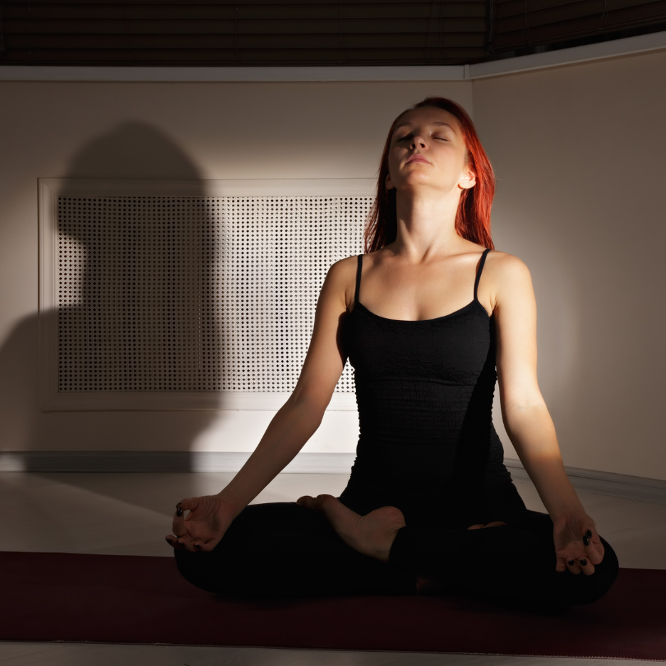 Woman seated cross-legged practicing hypopressive breathing with eyes closed in a dimly lit room