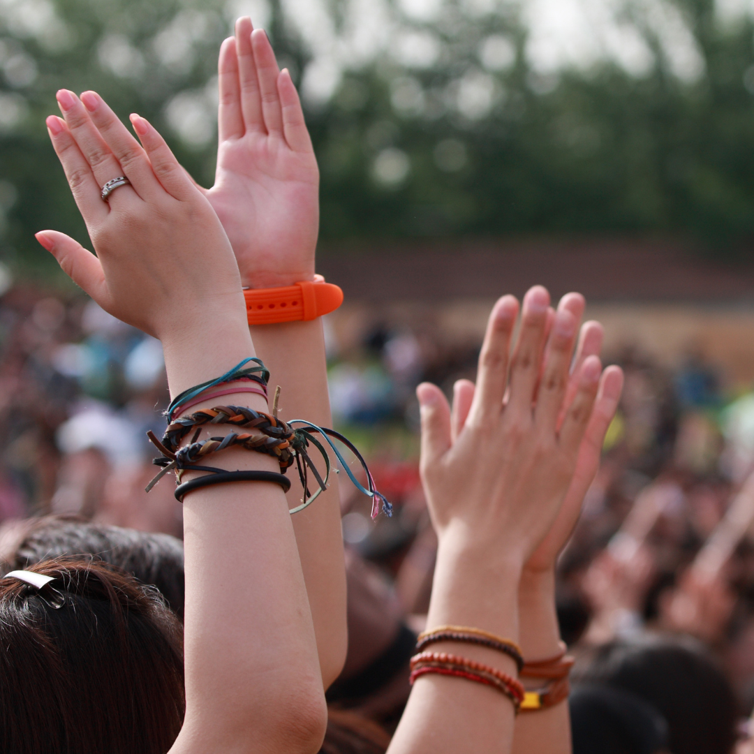 Festival crowd raising hands outdoors, focus on wrists with braided bracelets and an orange wristband