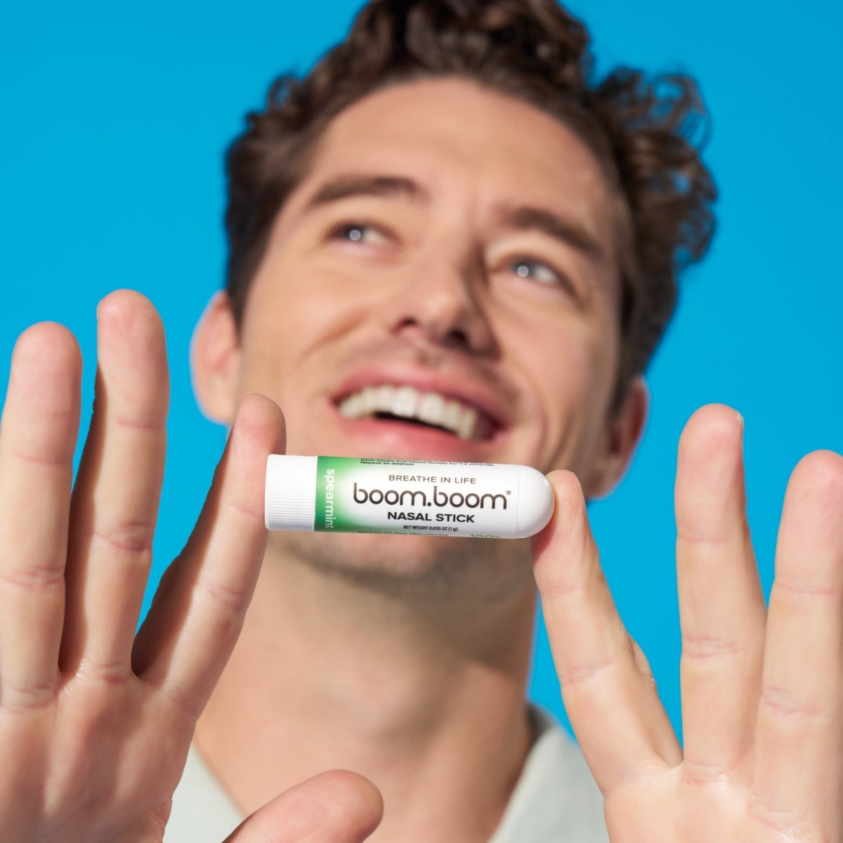 Man smiling and holding a BoomBoom nasal stick near his face against a bright blue background