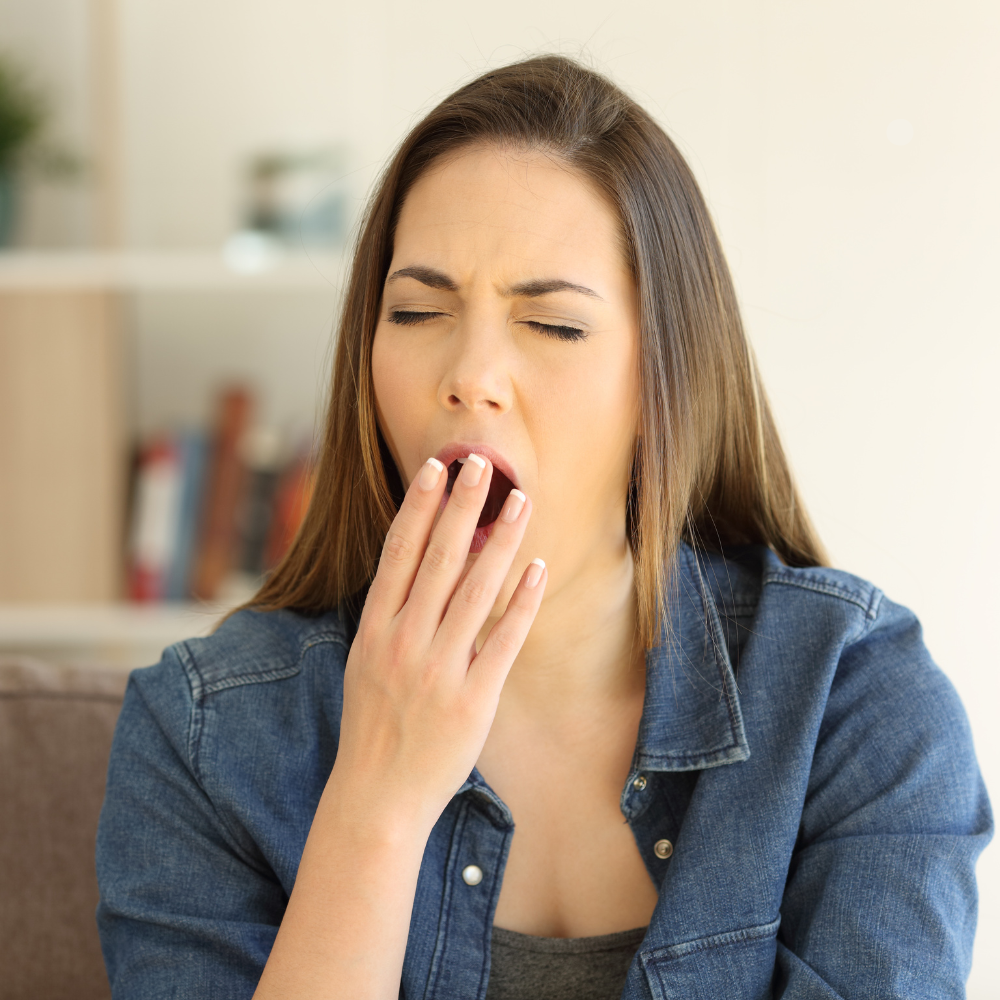 Young woman yawning with her hand over her mouth on a couch in a living room