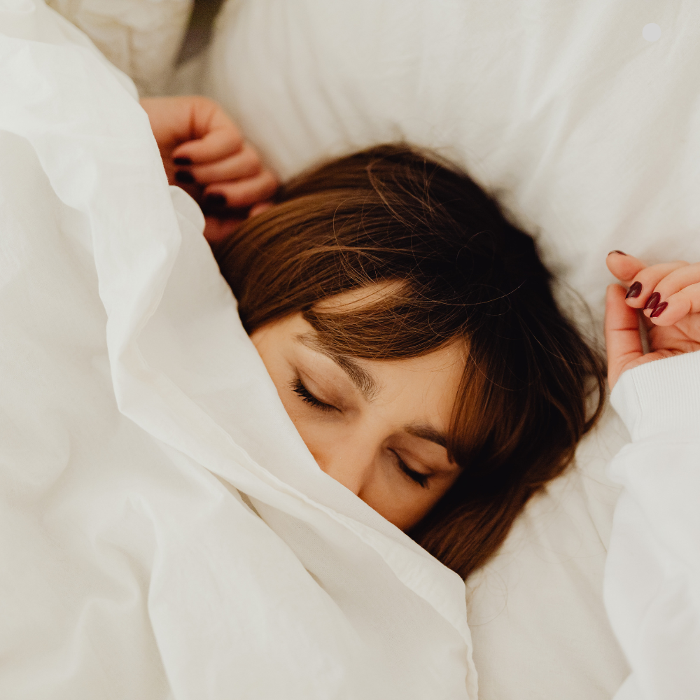 Person sleeping with eyes closed, face partially covered by a white duvet in a cozy bed