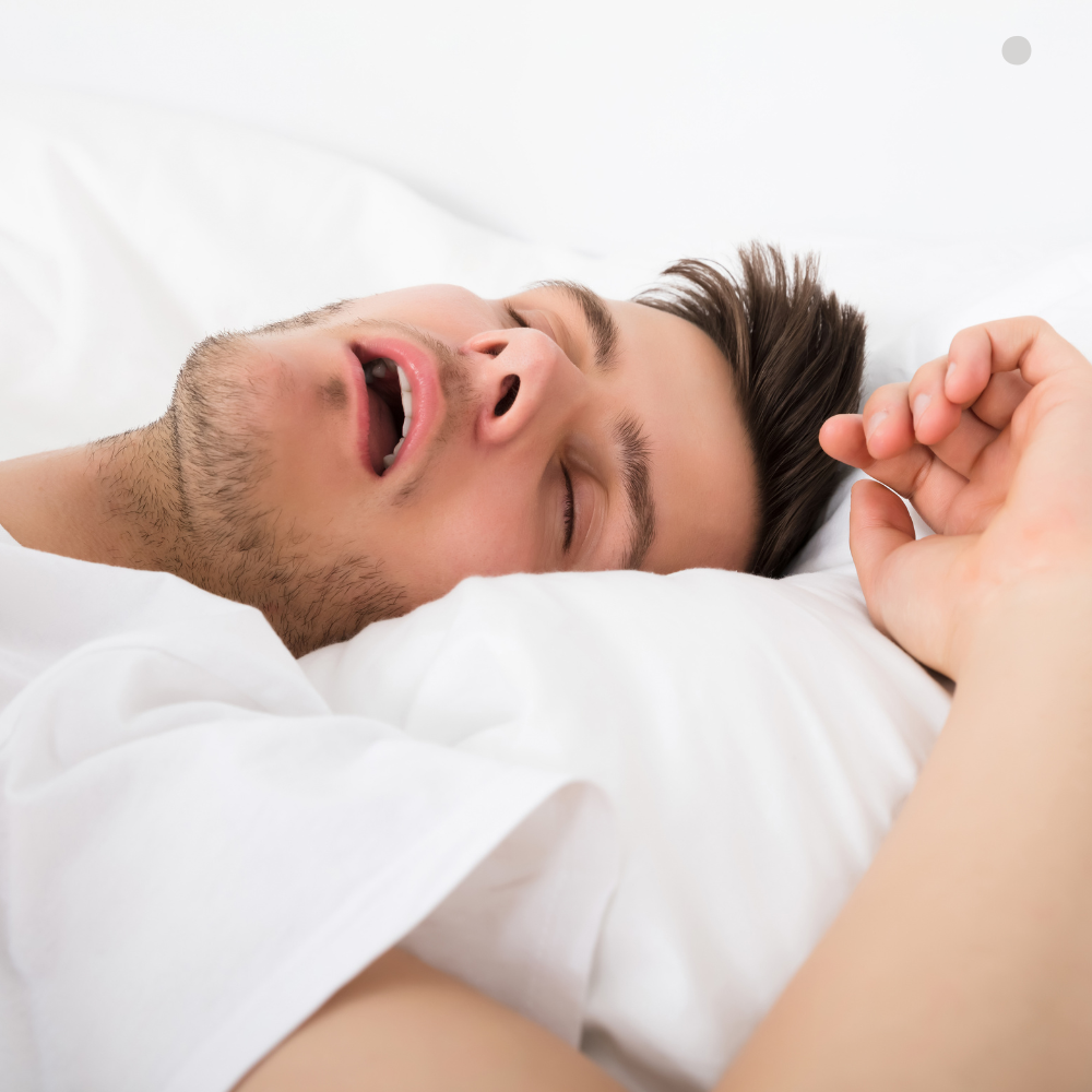 Man sleeping with mouth open on white bedding, appearing to snore