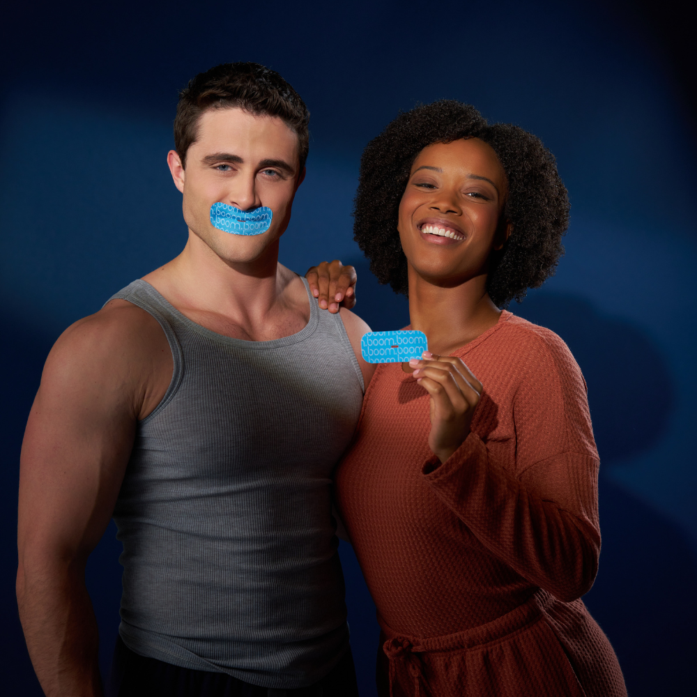 Man wearing BoomBoom Mouth Tape over closed lips beside a smiling woman holding a strip