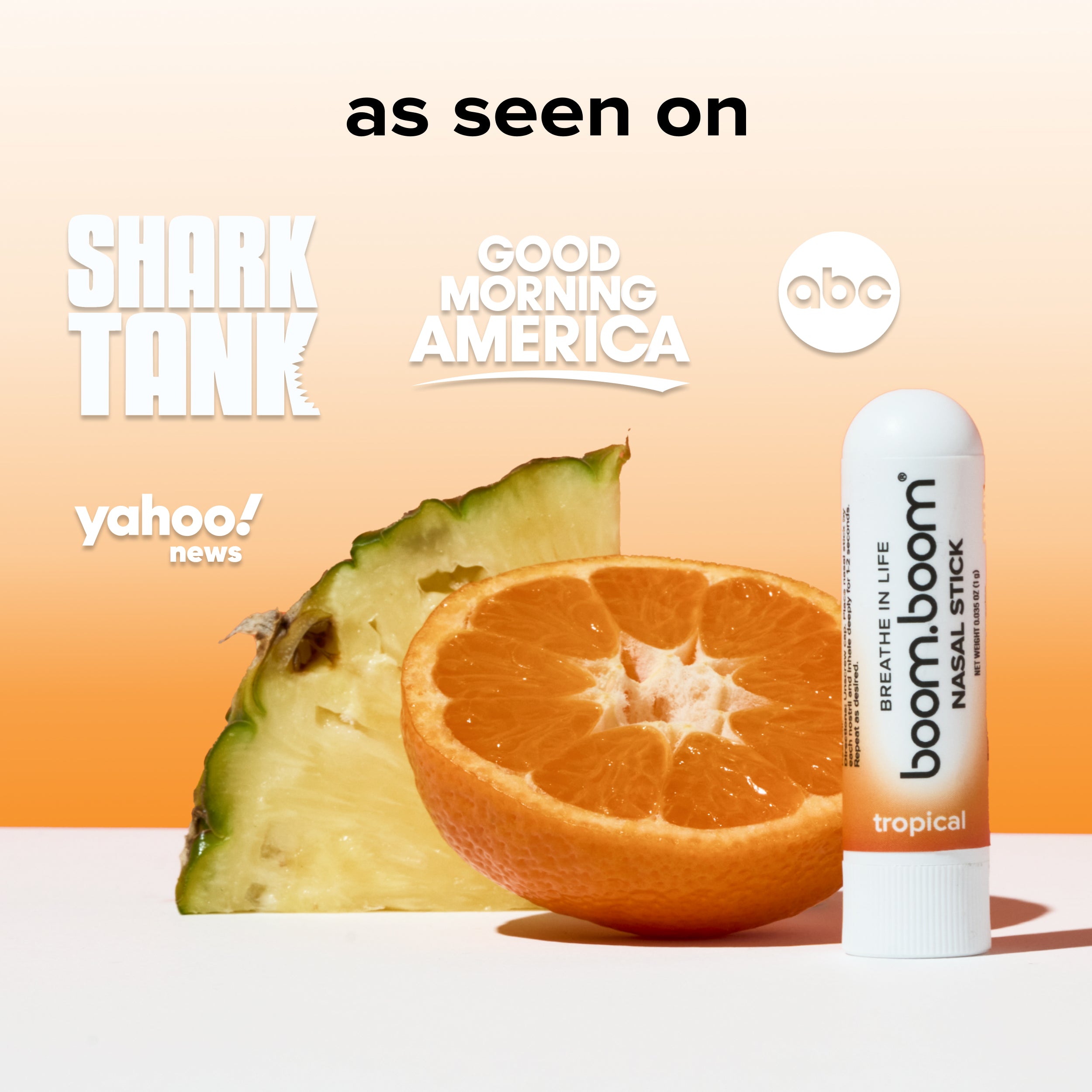 Right side view of BoomBoom Tropical nasal stick showcasing the white tube and tropical label with sliced orange and pineapple on a peach gradient background